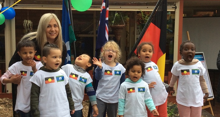 Educator surrounded by children wearing t shirts with Aboriginal and Torres strait Islander flags